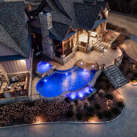a freeform corner pool from above at night that has purple pool lighting