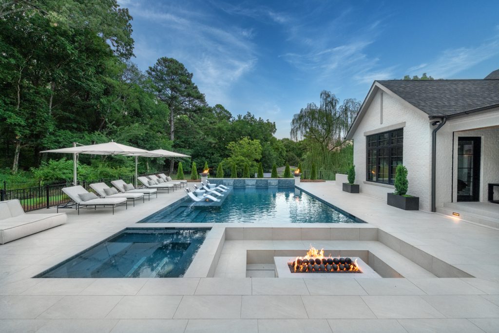 Luxury outdoor living space with inground pool, fire feature, and lounge seating by Burleson Master Pools Design Center